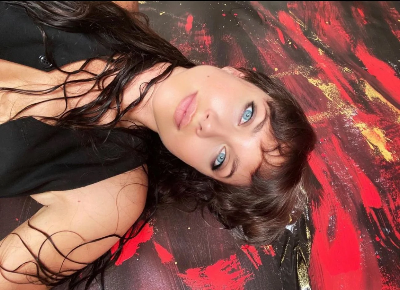 Maiara lying on Cadmium, her red, black and gold painting